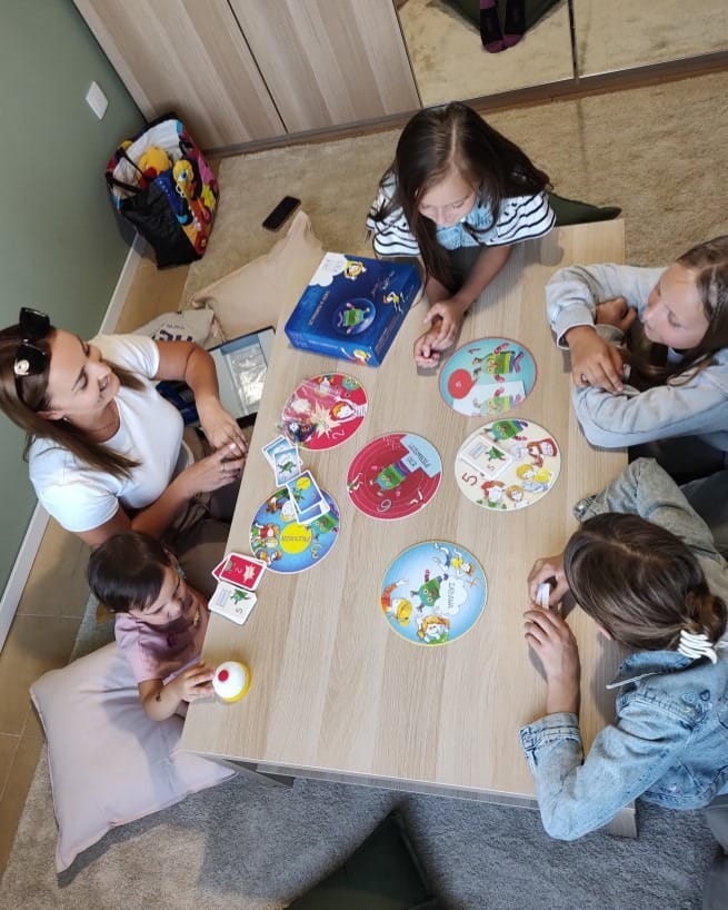 Grupa dzieci bawi się przy stole, układając puzzle w radosnej atmosferze wspólnej zabawy.